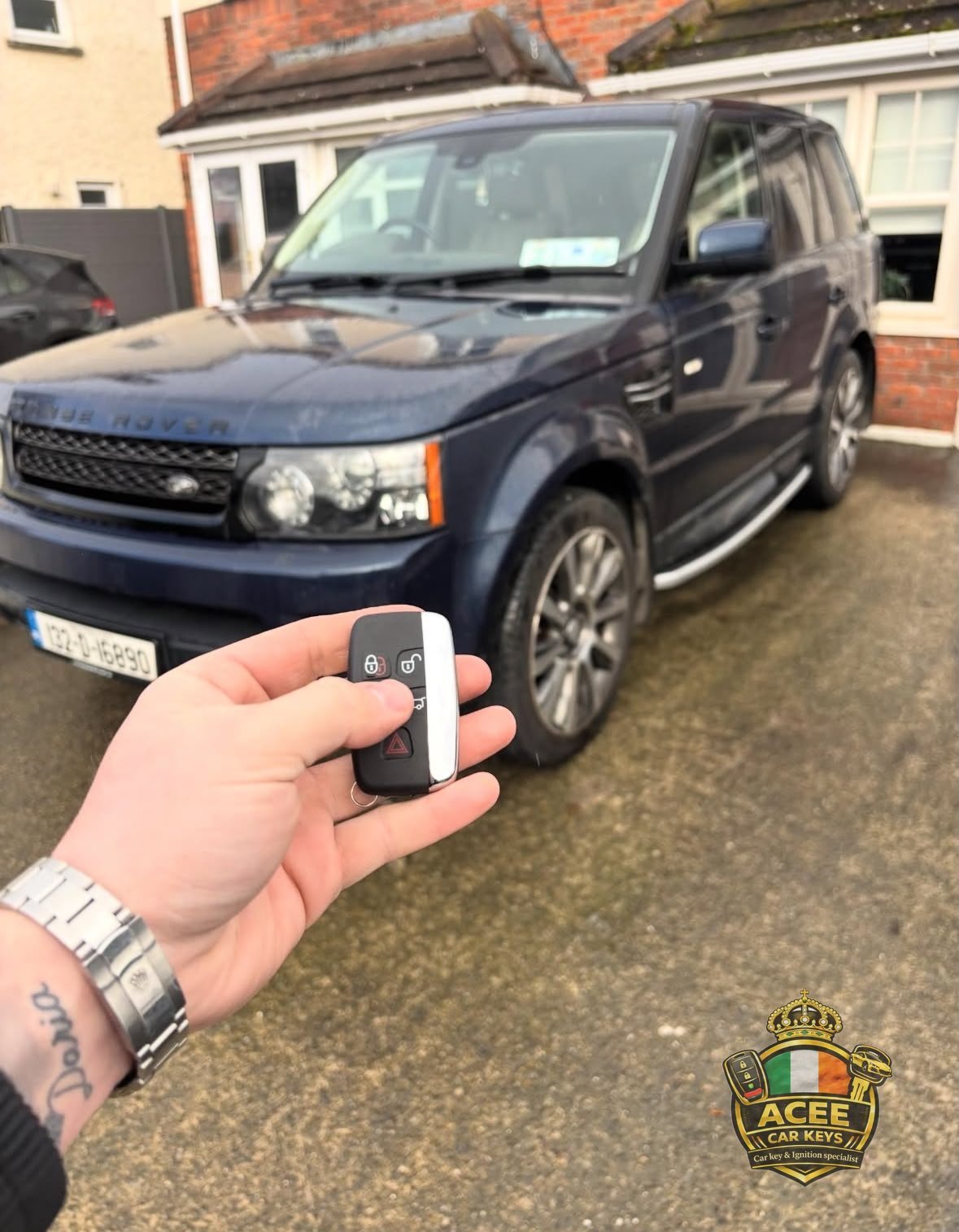 Person holding a car key fob in front of a dark blue Range Rover in a driveway
